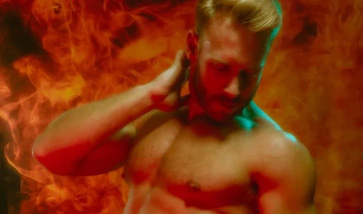 Shirtless muscular man posing against fiery orange background, highlighting athletic physique